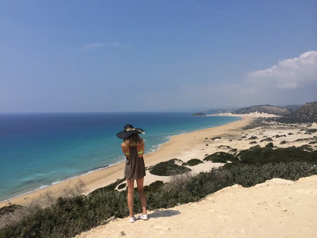 Kvinne med hatt ser utover en lang strand